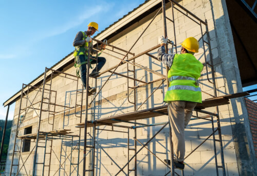 Lavoratori edili in uniforme e con equipaggiamento di sicurezza che lavorano su un ponteggio in un cantiere edile.