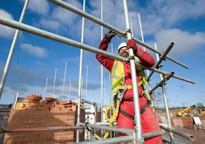 Operaio con imbracatura di sicurezza monta un ponteggio